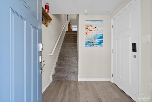 entrance foyer featuring stairs, wood finished floors, baseboards, and a textured ceiling