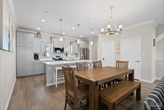 dining area featuring visible vents, crown molding, baseboards, light wood-type flooring, and a notable chandelier