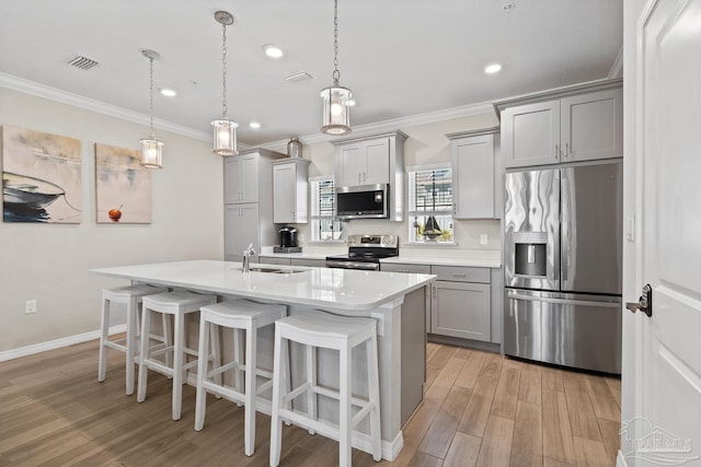 kitchen with a breakfast bar area, a sink, gray cabinetry, light countertops, and stainless steel appliances