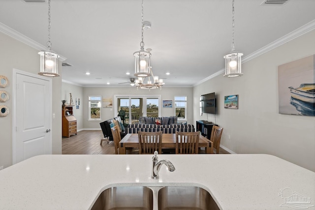 kitchen featuring decorative light fixtures, open floor plan, ornamental molding, wood finished floors, and a sink