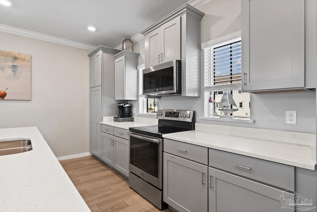 kitchen with gray cabinetry, light wood-style flooring, ornamental molding, appliances with stainless steel finishes, and baseboards