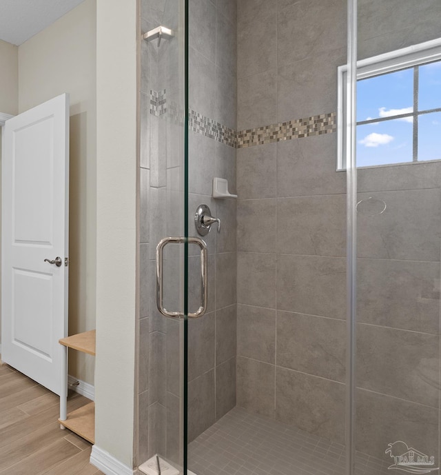 full bathroom with a stall shower, baseboards, and wood finished floors