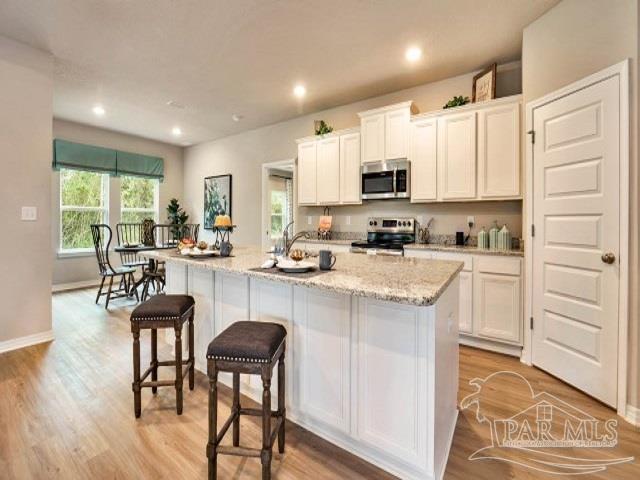 kitchen with light stone countertops, light hardwood / wood-style floors, a center island with sink, white cabinets, and appliances with stainless steel finishes