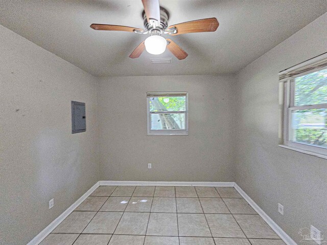 tiled empty room with electric panel, plenty of natural light, and ceiling fan