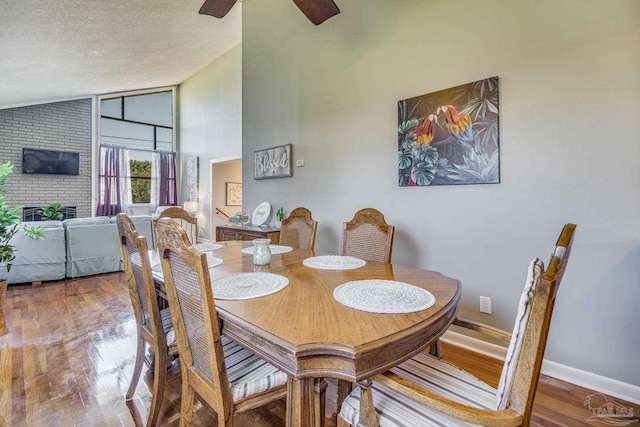 dining space with a textured ceiling, ceiling fan, brick wall, hardwood / wood-style flooring, and high vaulted ceiling