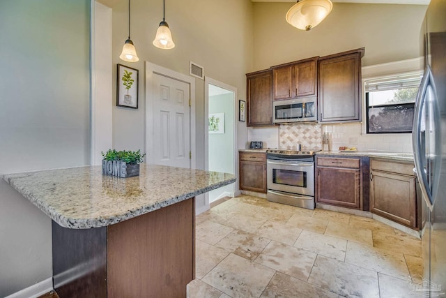 kitchen with light tile patterned floors, backsplash, light stone counters, appliances with stainless steel finishes, and pendant lighting