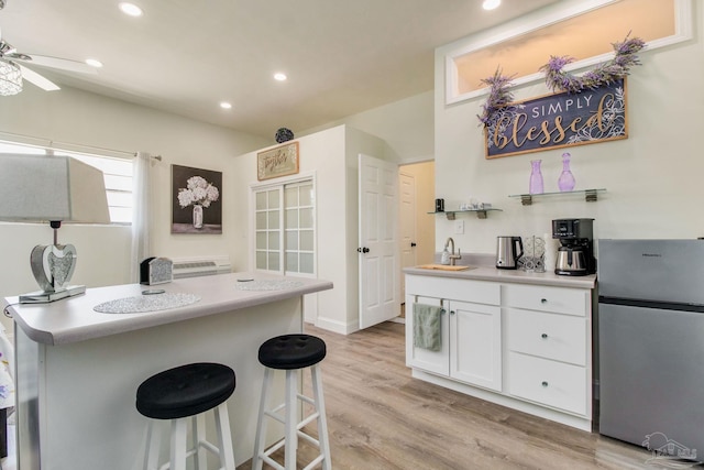 kitchen featuring light hardwood / wood-style flooring, white cabinets, a kitchen breakfast bar, ceiling fan, and stainless steel fridge