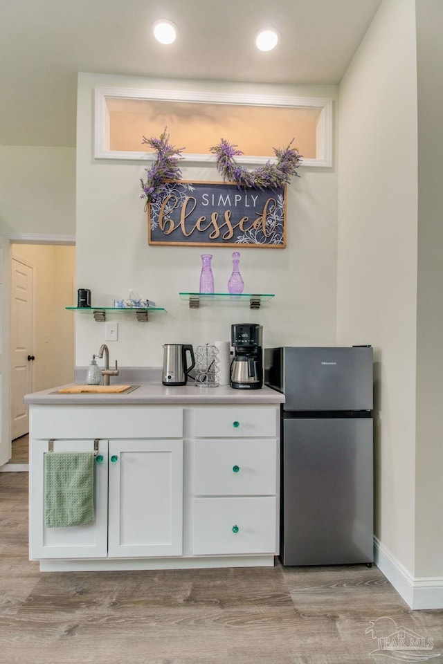 bar featuring sink, stainless steel refrigerator, white cabinets, and light wood-type flooring