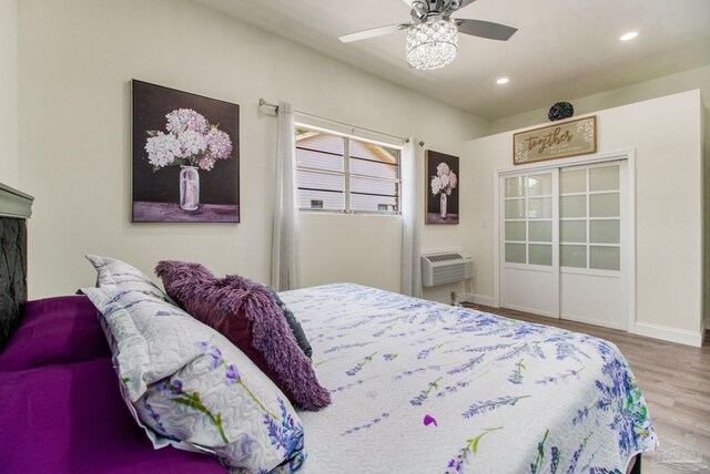 bedroom with wood-type flooring, a wall unit AC, and ceiling fan