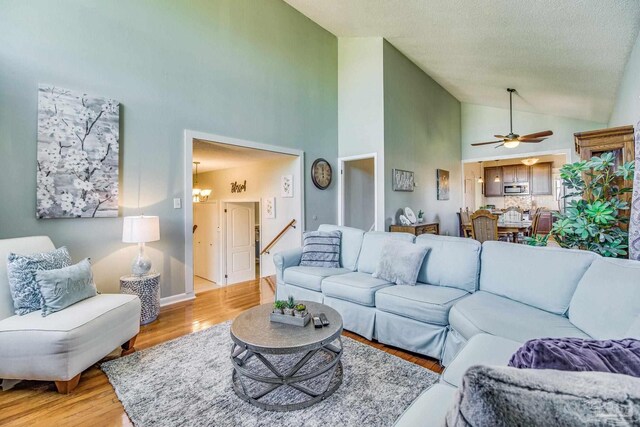 living room featuring high vaulted ceiling, a textured ceiling, ceiling fan, and light hardwood / wood-style floors