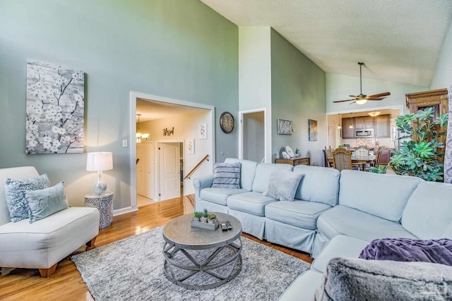 living room featuring a textured ceiling, ceiling fan with notable chandelier, high vaulted ceiling, and light hardwood / wood-style flooring