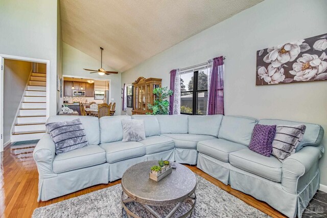 living room with high vaulted ceiling, light wood-type flooring, ceiling fan, and a textured ceiling