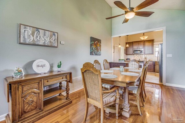 dining space with light hardwood / wood-style flooring, ceiling fan, and high vaulted ceiling