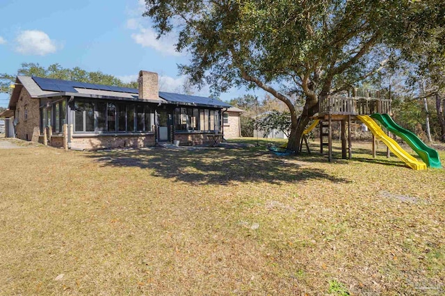 back of property featuring a yard, solar panels, a sunroom, and a playground