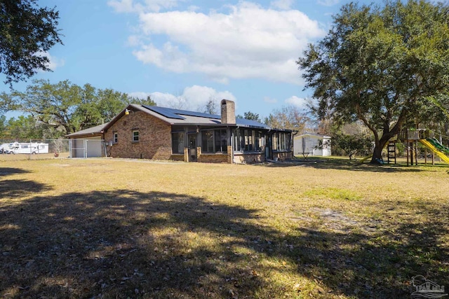 rear view of property featuring a playground, a lawn, a sunroom, and solar panels