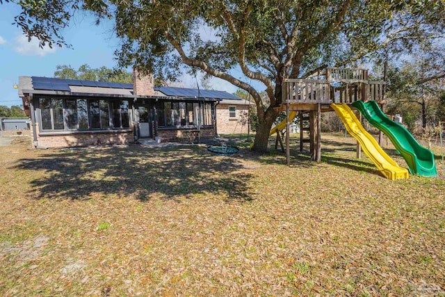 back of property featuring a lawn, a playground, a sunroom, and solar panels