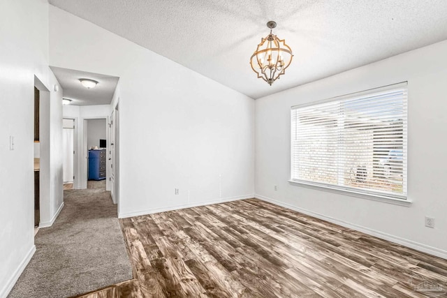 empty room with a textured ceiling, lofted ceiling, dark wood-type flooring, and an inviting chandelier