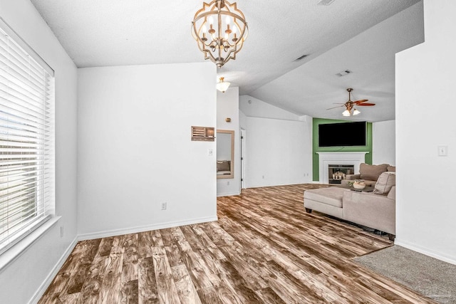 unfurnished living room with hardwood / wood-style floors, ceiling fan with notable chandelier, a textured ceiling, and vaulted ceiling