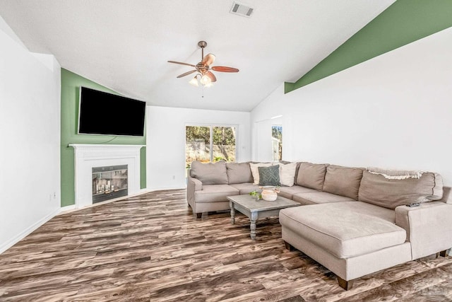 living room with visible vents, dark wood finished floors, a glass covered fireplace, ceiling fan, and vaulted ceiling