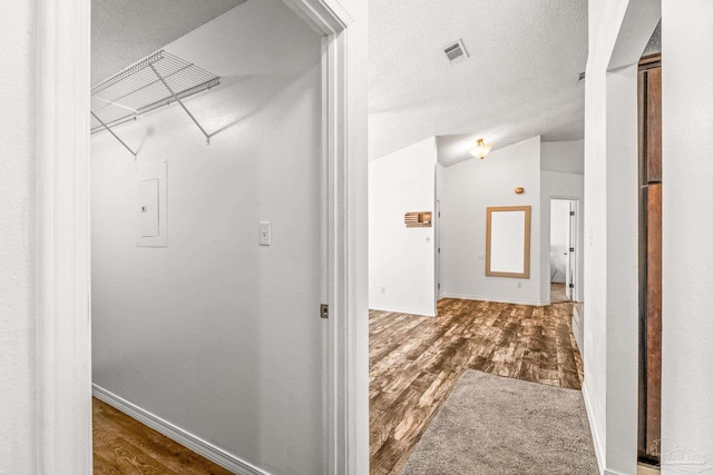 hallway with dark hardwood / wood-style floors, lofted ceiling, and a textured ceiling