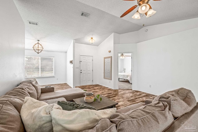 living room featuring wood-type flooring, a textured ceiling, an inviting chandelier, and lofted ceiling