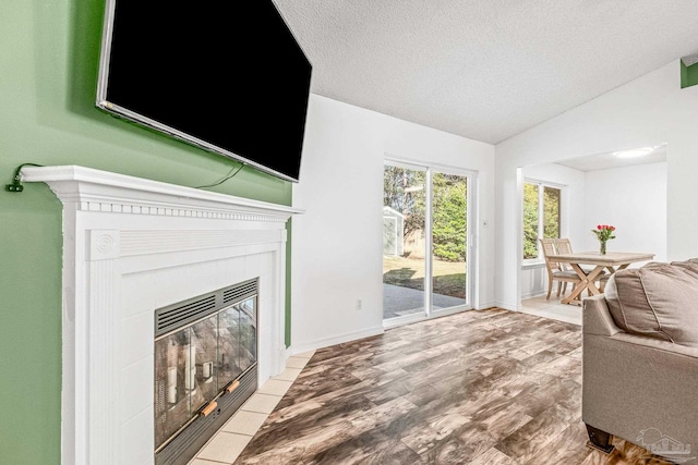 living room with a textured ceiling, a tile fireplace, vaulted ceiling, and hardwood / wood-style flooring