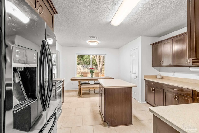 kitchen featuring a center island, black fridge with ice dispenser, dark brown cabinetry, and light tile patterned flooring