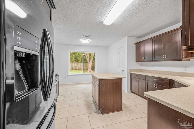 kitchen with black fridge, light countertops, a kitchen island, and dark brown cabinetry