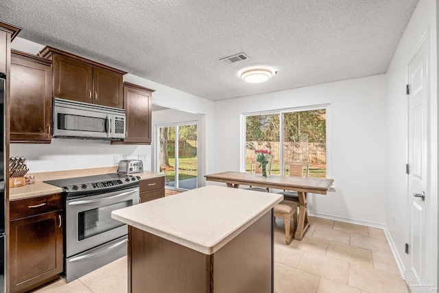 kitchen featuring a center island, stainless steel appliances, a textured ceiling, dark brown cabinets, and light tile patterned floors