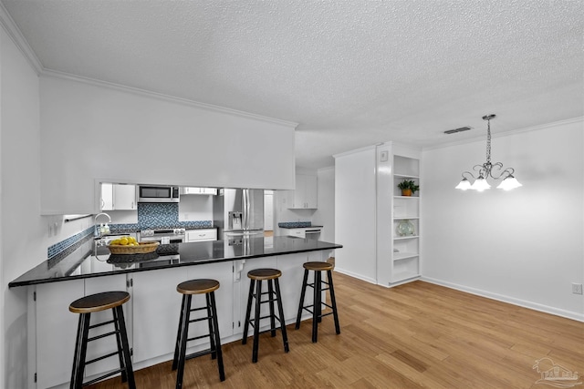 1213 Tecumseh Pl, Pensacola, FL 32514 - kitchen with appliances with stainless steel finishes, a peninsula, ornamental molding, white cabinetry, and a textured ceiling