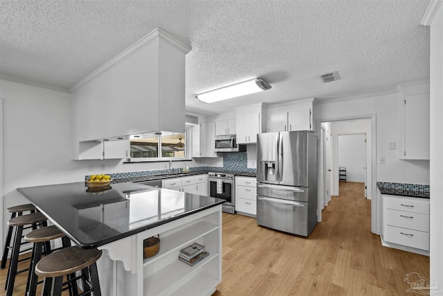 1213 Tecumseh Pl, Pensacola, FL 32514 - kitchen featuring appliances with stainless steel finishes, a peninsula, dark countertops, white cabinetry, and light wood-type flooring