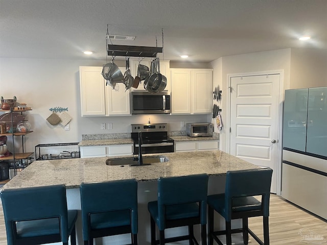 kitchen with light stone countertops, white cabinetry, light wood-type flooring, and appliances with stainless steel finishes