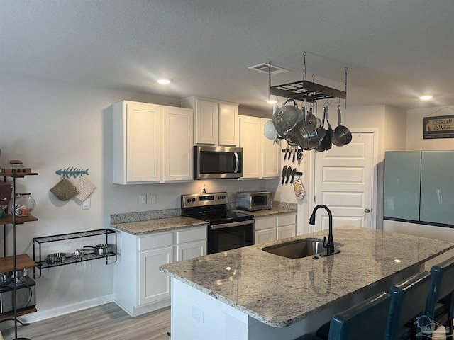 kitchen featuring a sink, visible vents, light wood-style flooring, white cabinets, and appliances with stainless steel finishes