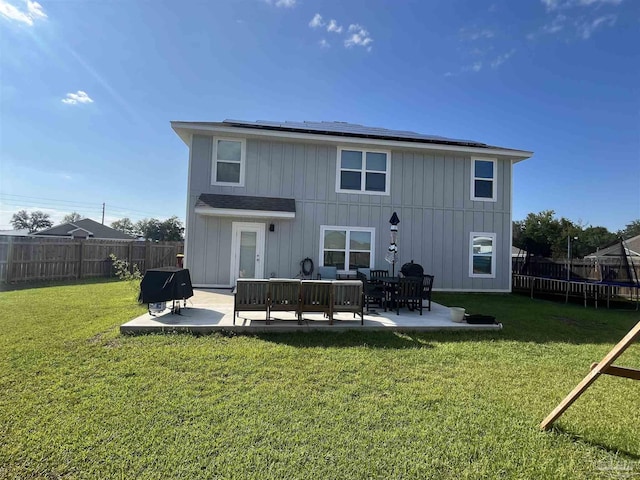 back of property with a trampoline, a patio, solar panels, and a lawn