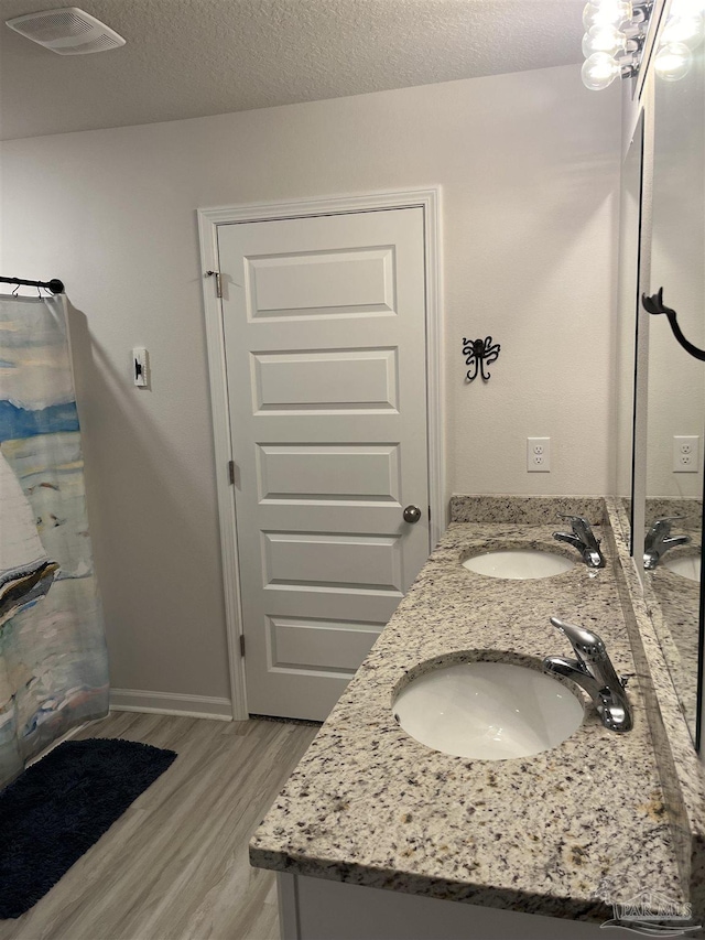 bathroom featuring visible vents, double vanity, a sink, and wood finished floors
