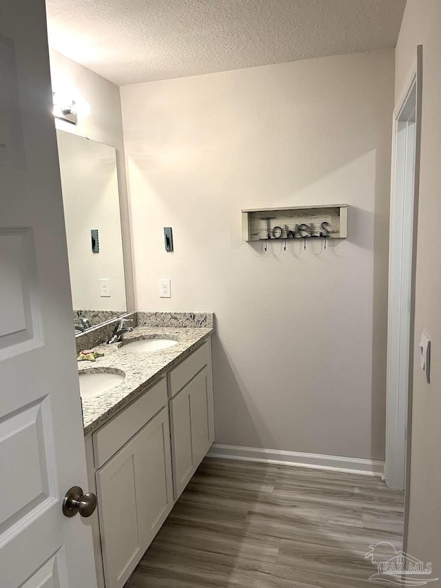 bathroom featuring double vanity, a textured ceiling, wood finished floors, and a sink