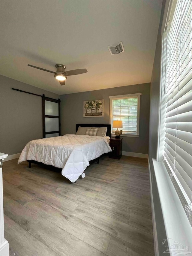 bedroom with a barn door, ceiling fan, and hardwood / wood-style flooring