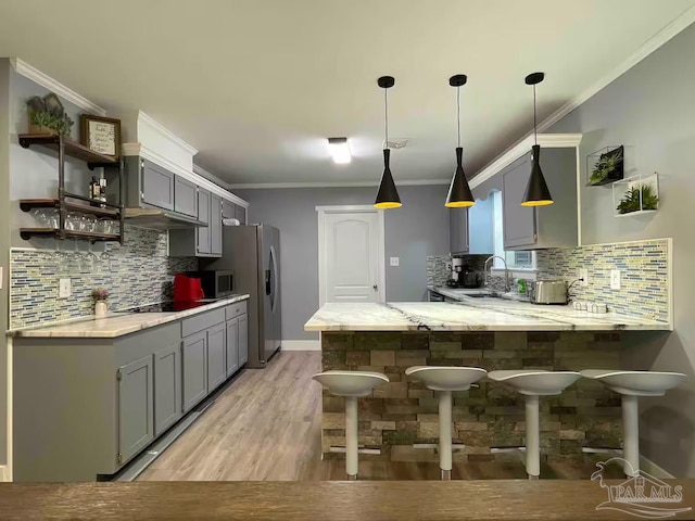 kitchen featuring light hardwood / wood-style flooring, kitchen peninsula, pendant lighting, decorative backsplash, and appliances with stainless steel finishes