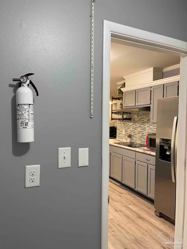 kitchen featuring stainless steel refrigerator with ice dispenser, backsplash, light hardwood / wood-style flooring, and black electric stovetop