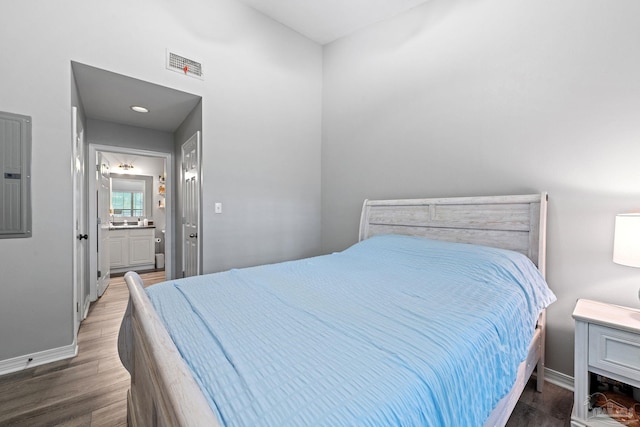 bedroom with wood finished floors, baseboards, connected bathroom, and electric panel