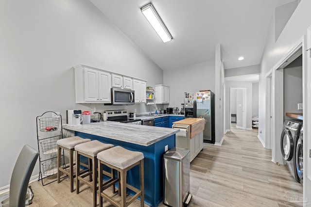 kitchen with appliances with stainless steel finishes, a peninsula, high vaulted ceiling, white cabinetry, and separate washer and dryer