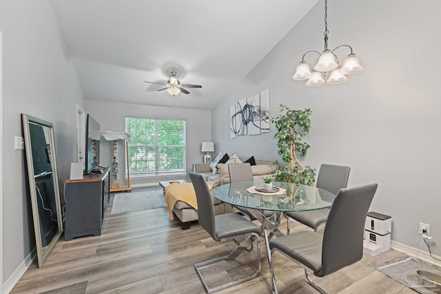 dining space featuring vaulted ceiling, light wood-style floors, a ceiling fan, a chandelier, and baseboards