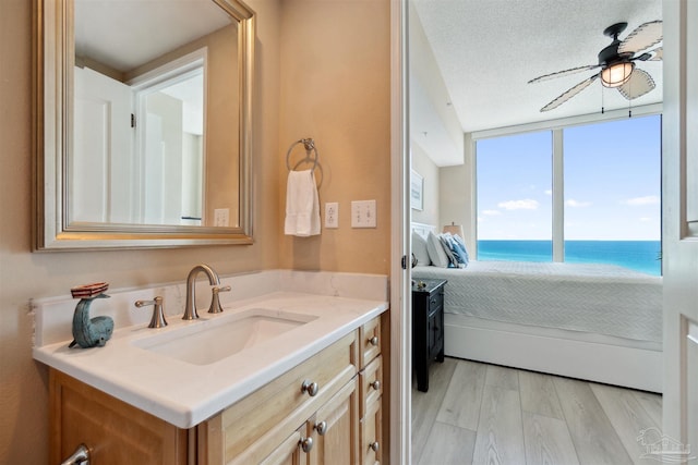 bathroom featuring a water view, a ceiling fan, vanity, ensuite bath, and a textured ceiling