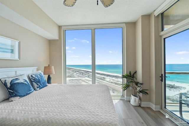 bedroom with a view of the beach, wood finished floors, a water view, and multiple windows