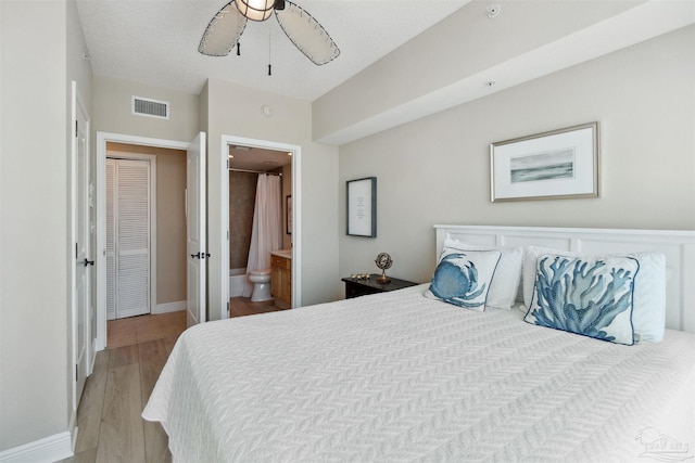 bedroom with light wood finished floors, ensuite bathroom, baseboards, visible vents, and a ceiling fan
