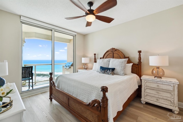 bedroom with light wood-style flooring, a water view, a wall of windows, a ceiling fan, and access to outside