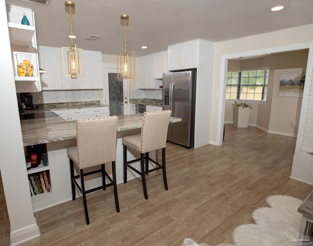 kitchen with white cabinets, appliances with stainless steel finishes, a breakfast bar, light wood-style floors, and backsplash