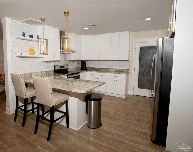 kitchen featuring appliances with stainless steel finishes, a peninsula, white cabinetry, wood finished floors, and visible vents