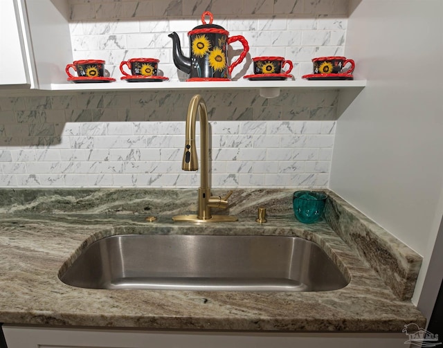 details featuring a sink, light stone counters, and backsplash