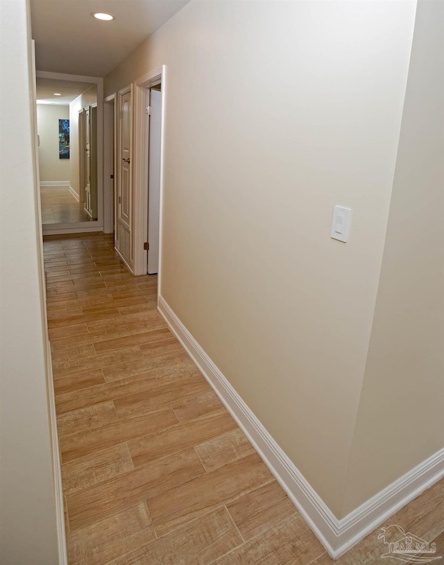 hallway featuring baseboards, light wood-type flooring, and recessed lighting